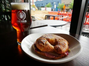 A ham and cheese croissant sandwich sitting next to a pint of IPA.